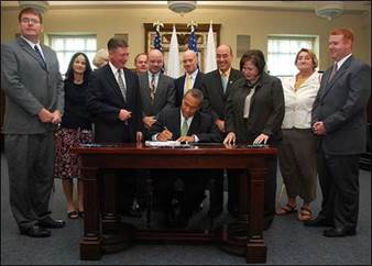 photo of Governor Patrick signing a law surrounded by other people in suits